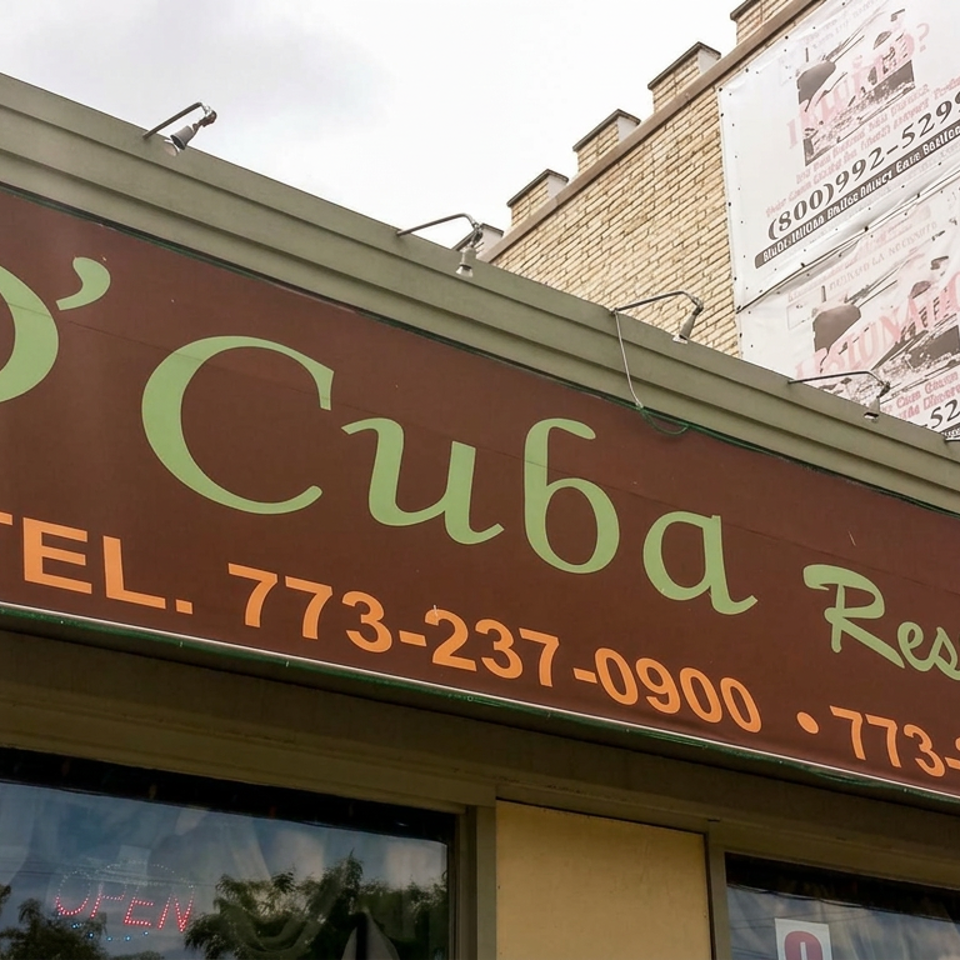 Street-facing D'Cuba Restaurant storefront displays its name and phone numbers beneath a brick building.